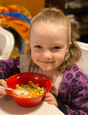 Child smiling with a bowl of cereal.