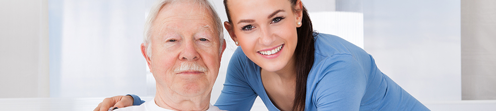 Young woman smiling with her arm around an older man lying in a bed.