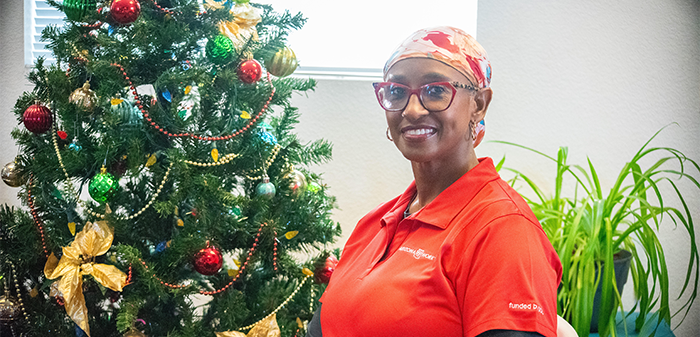 Person in a red polo shirt with glasses and a headscarf standing indoors.