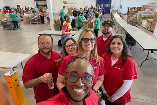A group of six people in red shirts posing indoors at an event.