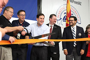 A group of people using a giant pair of scissors to cut through a ribbon