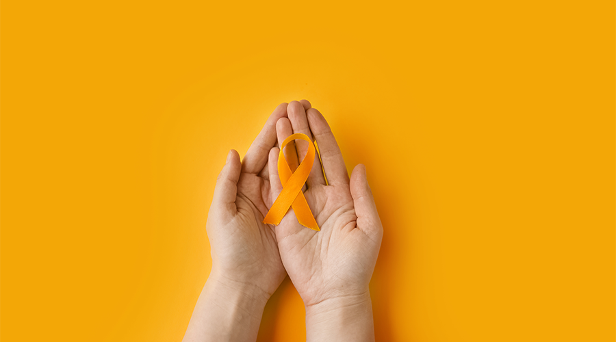 Hands holding an orange ribbon on an orange background. Concept of protection of children and adolescents from sexual violence and abuse.