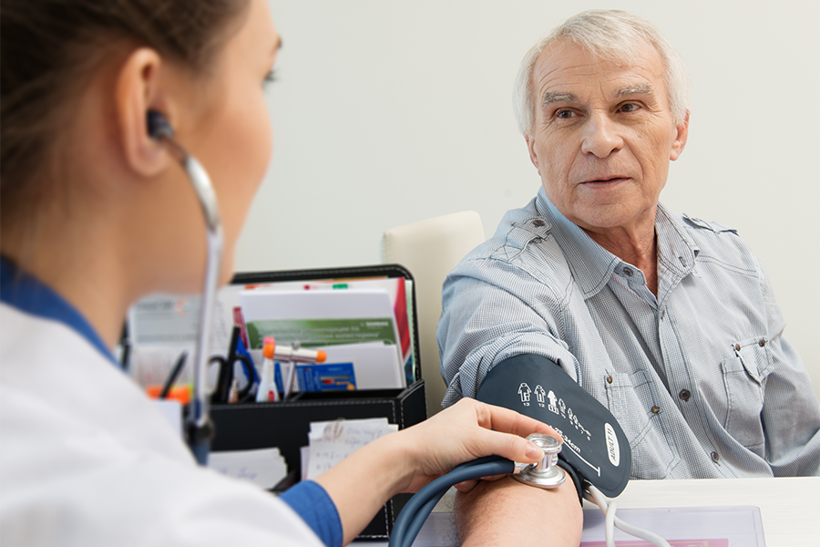 A healthcare professional takes the blood pressure of an older male patient.