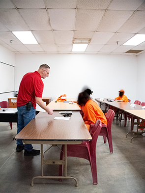 Classroom with people seated in orange clothing and a man standing near a table.