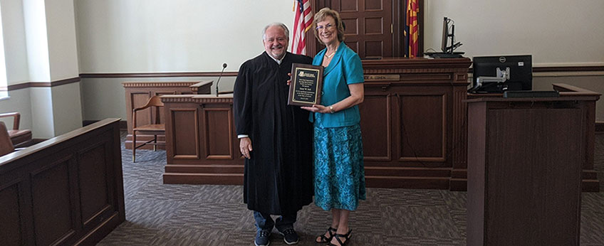 a woman holds an award while standing next to a judge