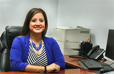 dark-haired woman sits at desk, smiling