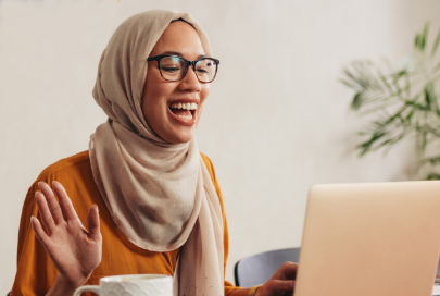 Woman with head scarf laughing at something on her computer.