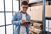 Young man holding a clipboard and checking inventory in a warehouse.