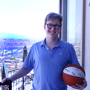 Young man stands on the backyard balcony cradling a basketball in his left hand.