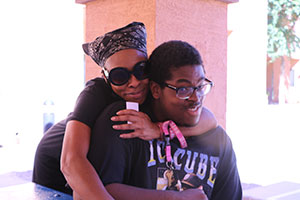 Woman, standing behind her son, gives him a big hug.