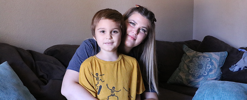 Young woman holds a young boy in her lap, looking straight ahead and smiling