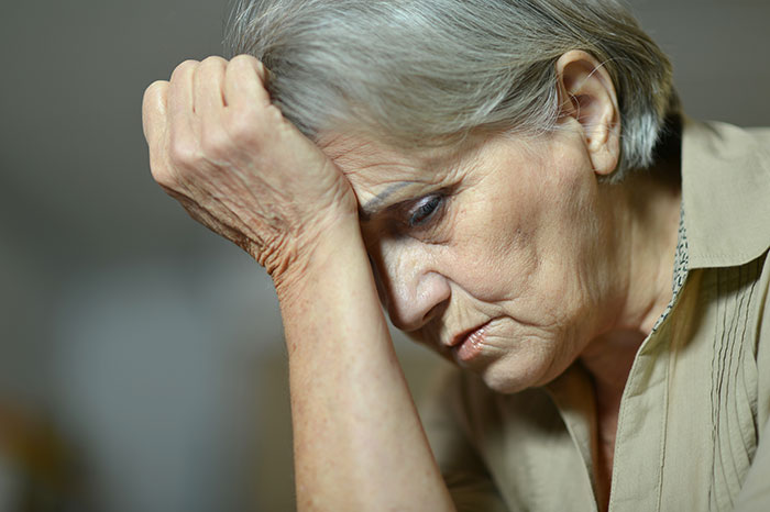 older, sad woman touching her palm to her forehead