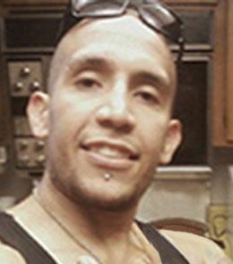 Man with shaved head wearing black sunglasses and black tank top