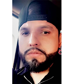 Male with a full beard wearing a backwards baseball cap