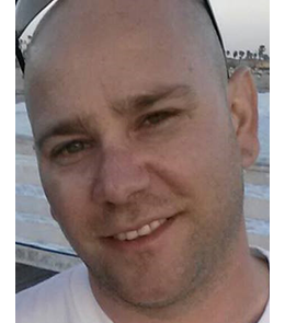 White male with bald head and brown eyes.