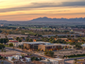 Aerial view of a cityscape at sunset with mountains in the background and colorful sky.