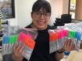a young girl smiles while holding plastic bags filled with colorful markers