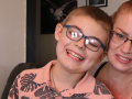 A smiling 12-year-old boy sits on his mother’s lap for a quick photo.