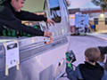 A young man handing a beverage to a child from a silver food truck.