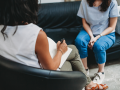 two women sit across from each other on sofas