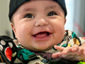 Smiling baby in an activity center with a red monkey toy.