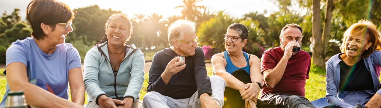 Group of older adults seated on the grass, talking together outdoors.