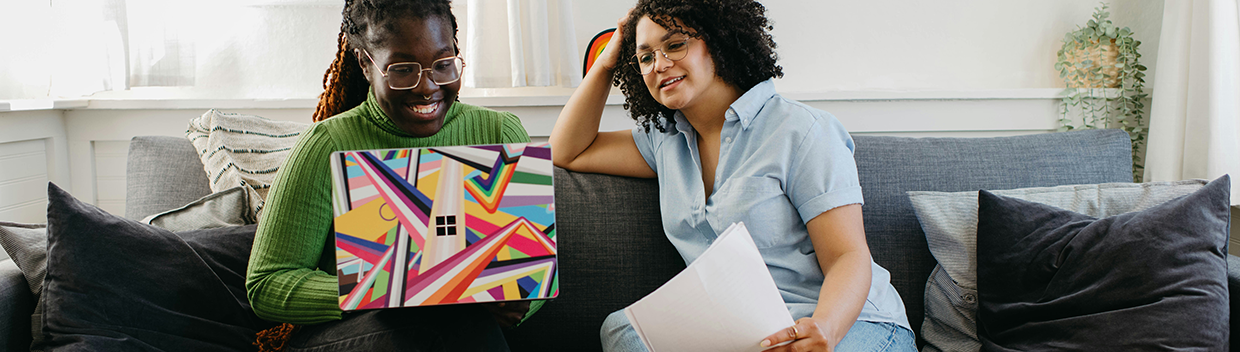 Two women sitting on a sofa looking at a laptop screen together.
