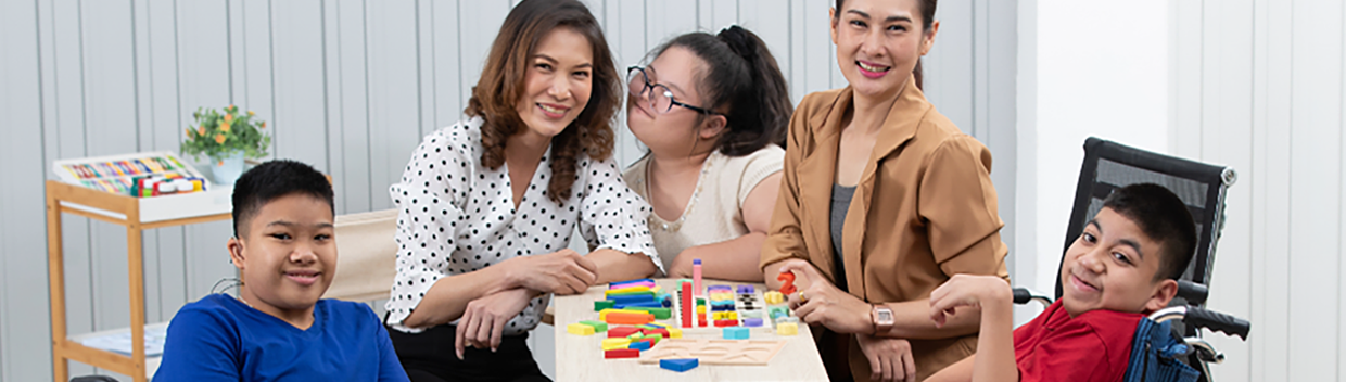 A group of five people, including three children and two women, gather around a table with blocks