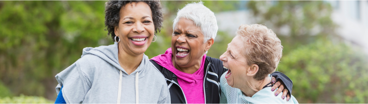 Three older women laugh and lean on each other