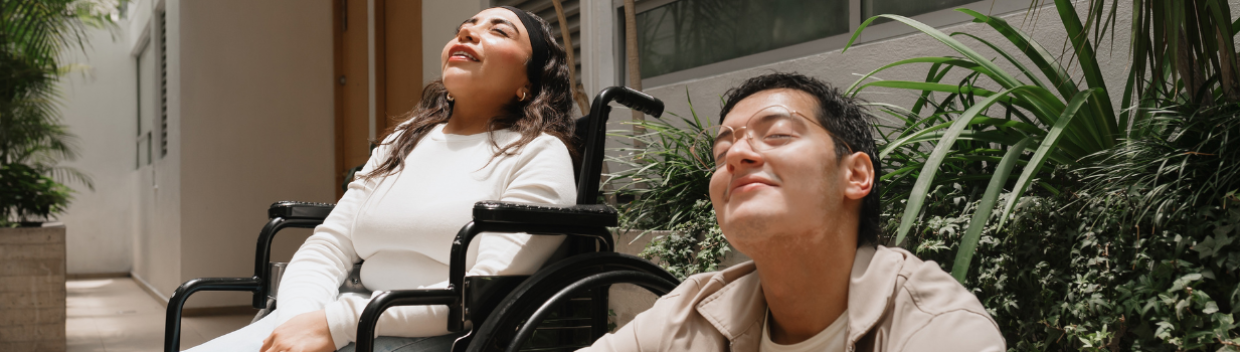 two young adults sitting outside a house; one is in a wheelchair