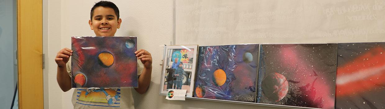 Young teen holds up one of his spray-painted artwork