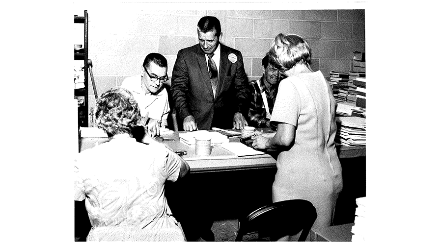 office workers stand around a man sitting at a desk