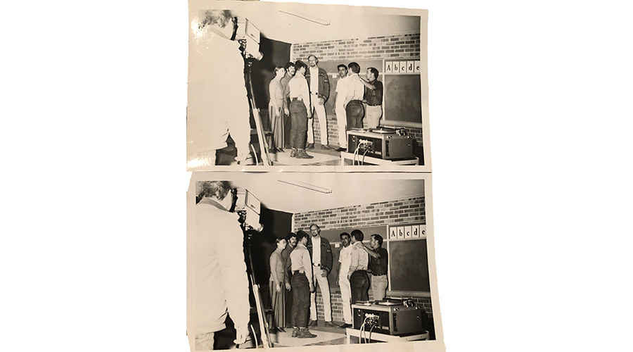 several men stand inside a workshop; a camera man stands in a corner