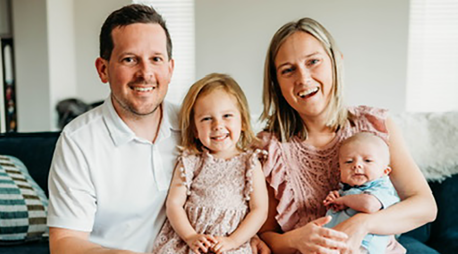 a little girl sitting on a man's lap and woman holding a baby