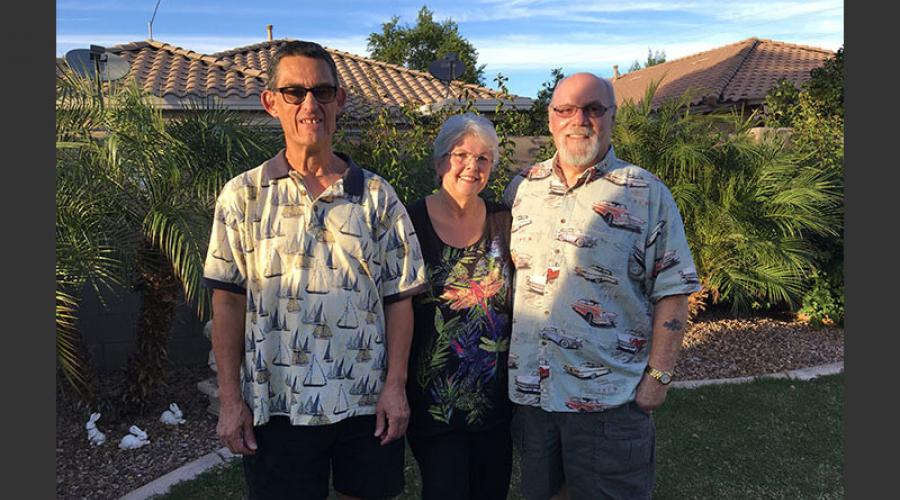 an older man wearing glasses stands next to an older man and woman in a backyard garden area.