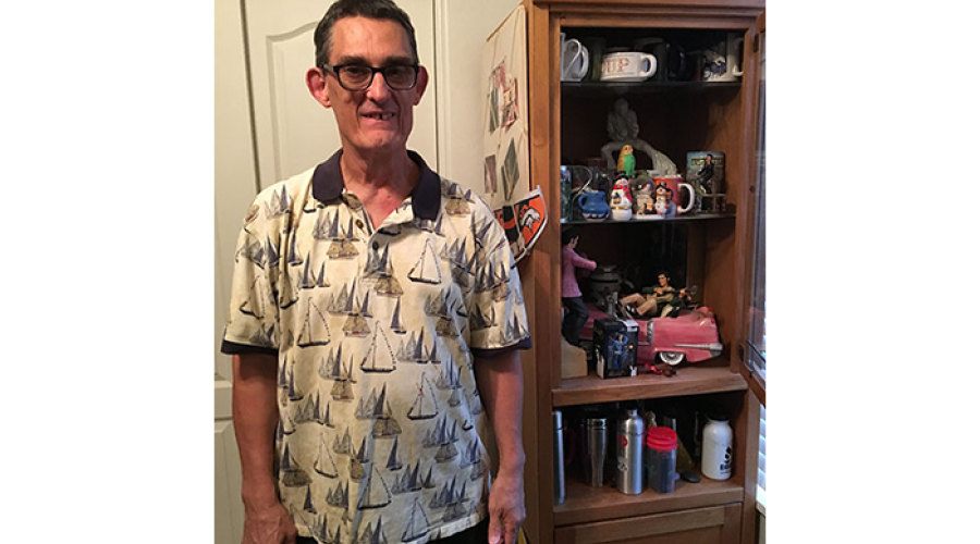 an older man wearing glasses is smiling; he is standing next to a wooden bookcase