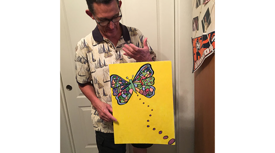 an older man holds a large bright and colorful drawing of a butterfly