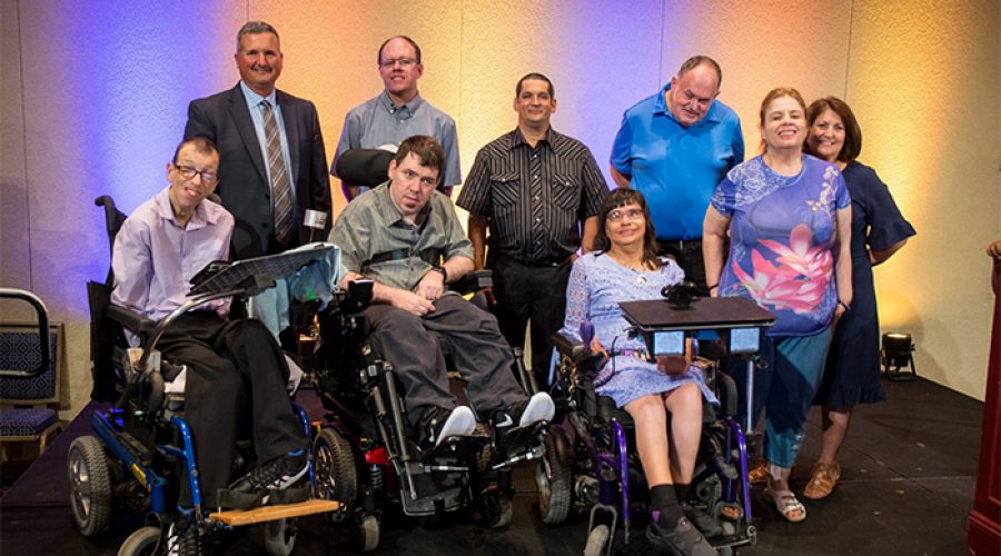 Six men and three women pose together for a picture. There are three individuals using wheel chairs in the front row, while the other participants stand in a row behind them.