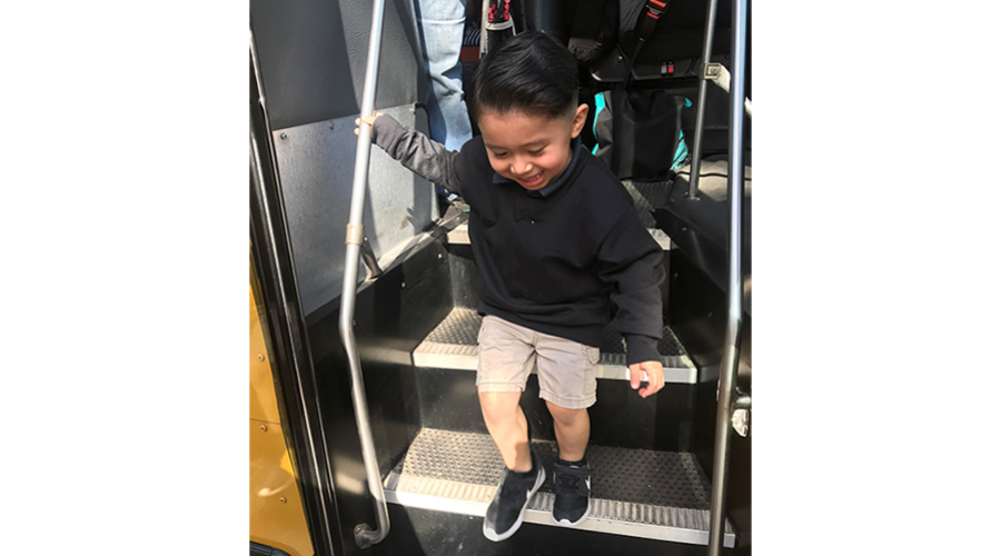 Toddler boy takes a step off the school bus on his first day of school.