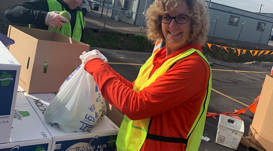 a woman wearing a bright yellow vest is placing a plastic bag on top of a stack of cardboard boxes