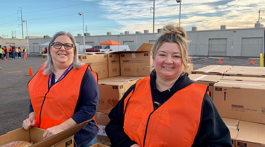 two women wearing bright orange vests are surrounded by cardboard boxes