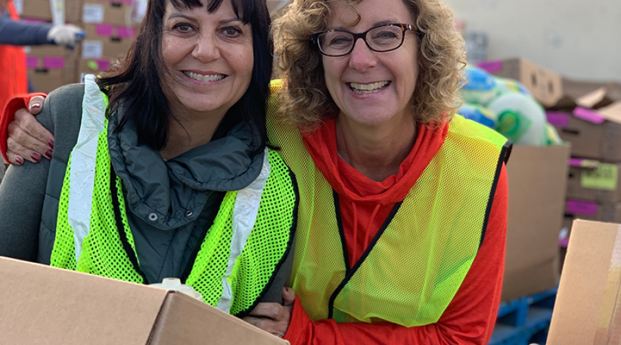 two women wearing bright yellow vests smile, posing for a photo