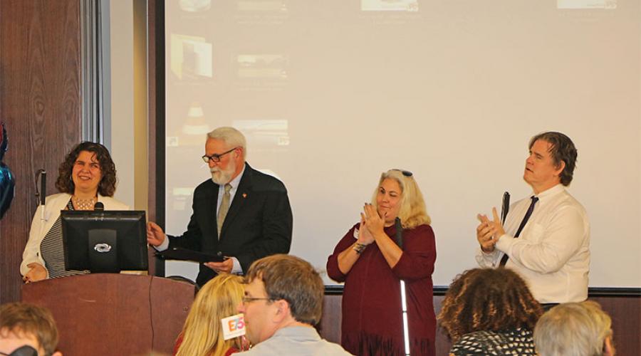 Two men and two women standing at a podium applauding