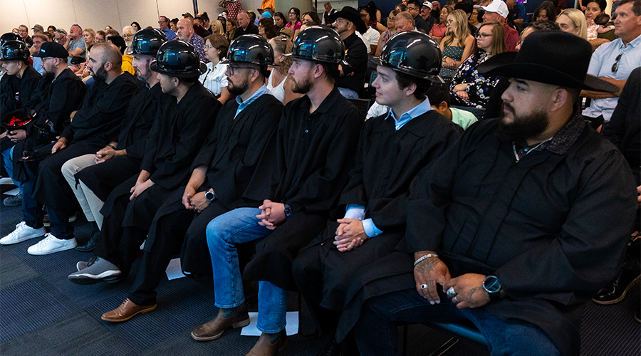 A row of graduates in black gowns and hard hats seated at a graduation ceremony.