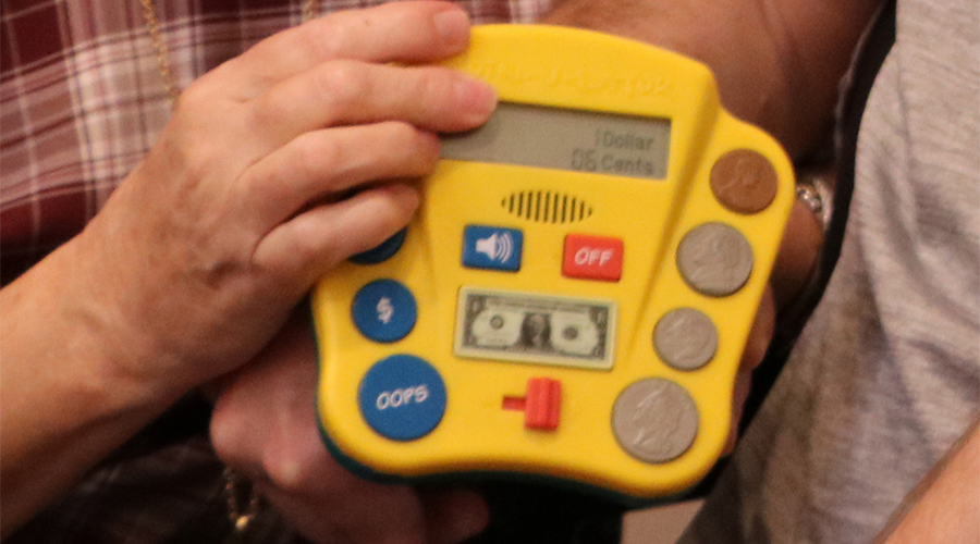 a hand holds up a learning device with a display area and buttons that resemble coins