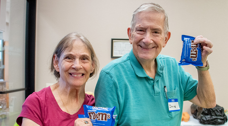 An older couple smiling while holding bags of peanut M&M's.
