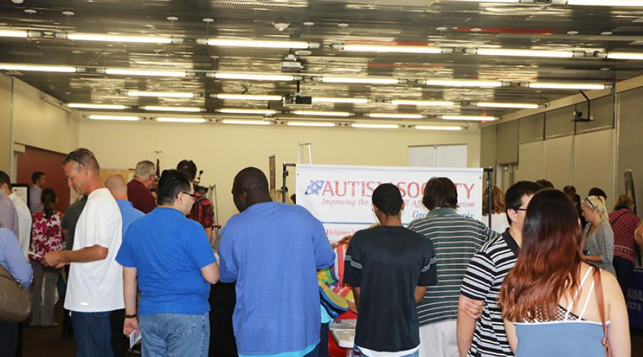 Male and female job seekers visiting tables set up by employers. A banner reading Autism Society in the background