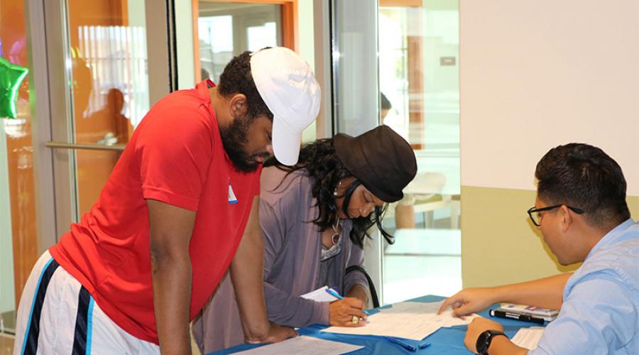 a woman and man stand at a counter, signing documents