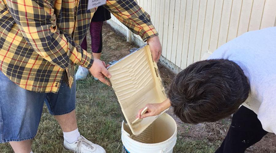 Man pours paint into a bucket outside of a home