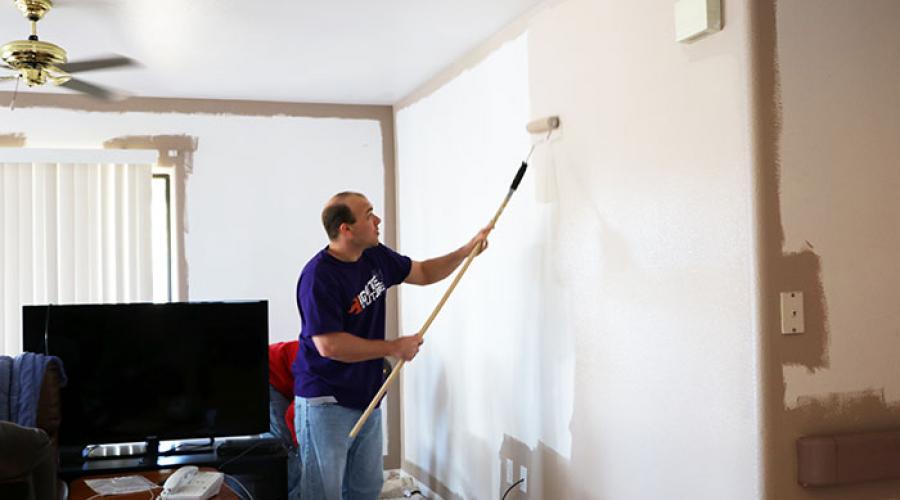 Man using roller to paint high on a wall